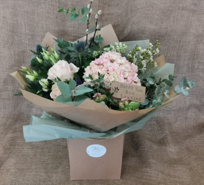 Blooming Gorgeous - A hand tied bouquet of florist choice flowers, presented in a Kraft gift bag and finished off with a luggage tag.